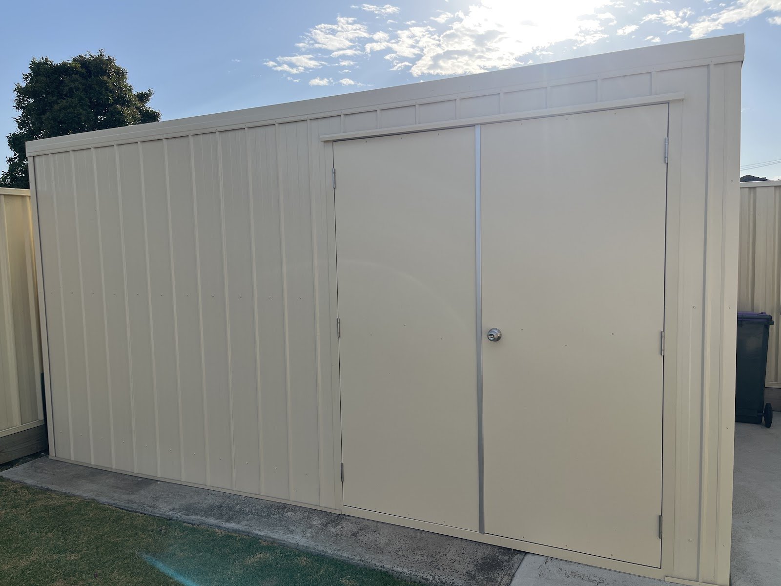 Cream colorbond garden shed with double doors built against a fence