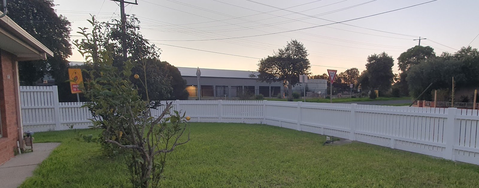 White picket fence wrapping around a front lawn at dusk