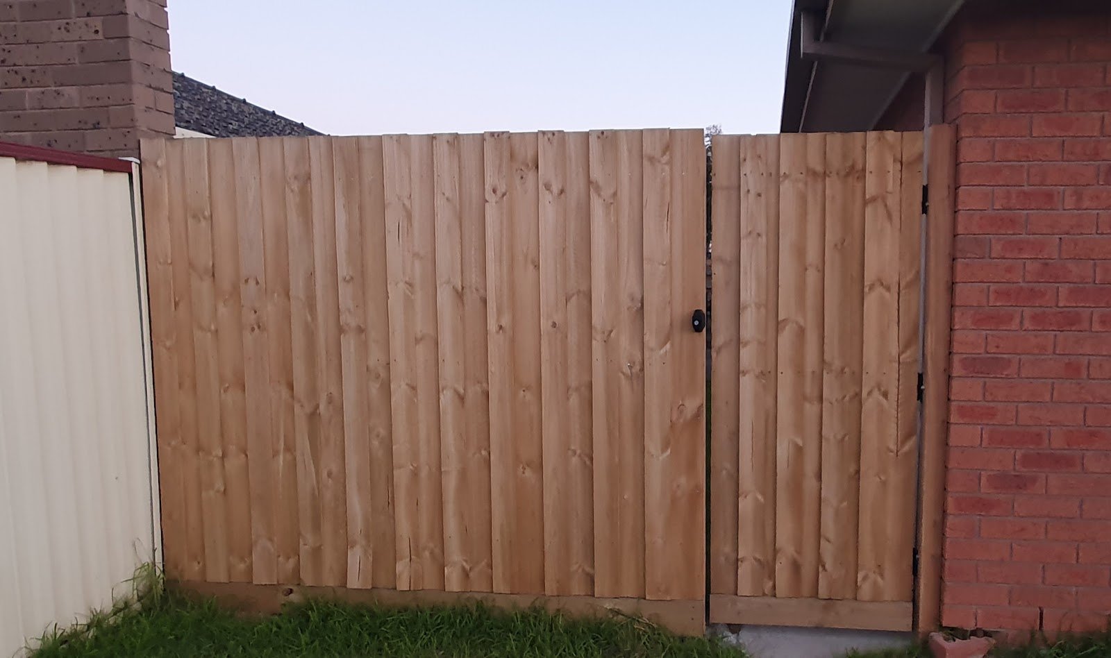 New timber paling fence and gate beside a red brick house
