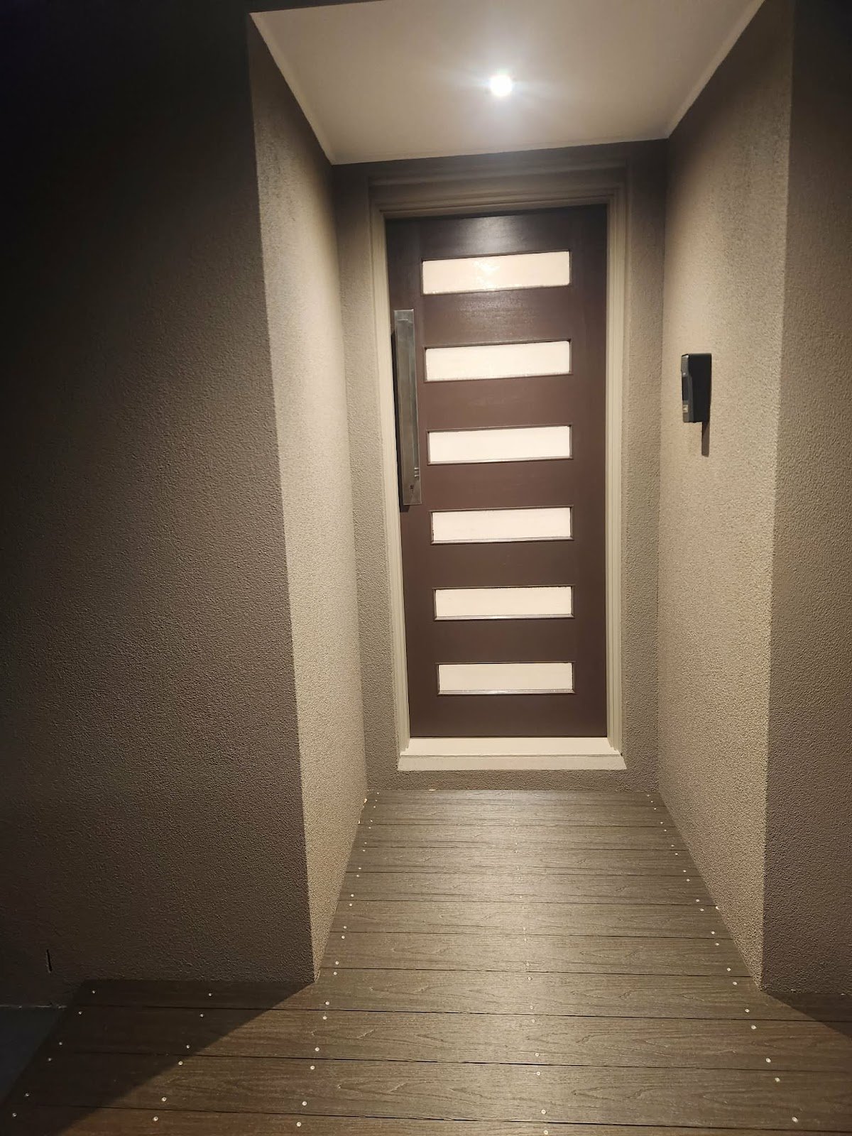 Front entry at night with new door and timber decking lit by step lights